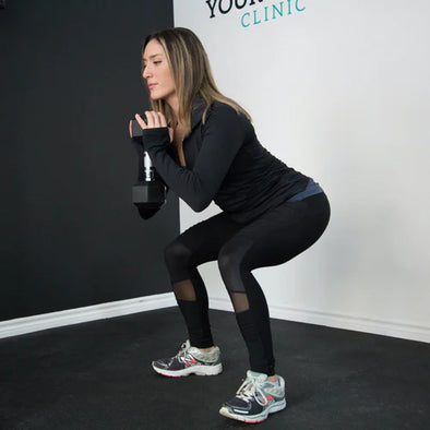 A woman doing a squat while holding a dumbbell
