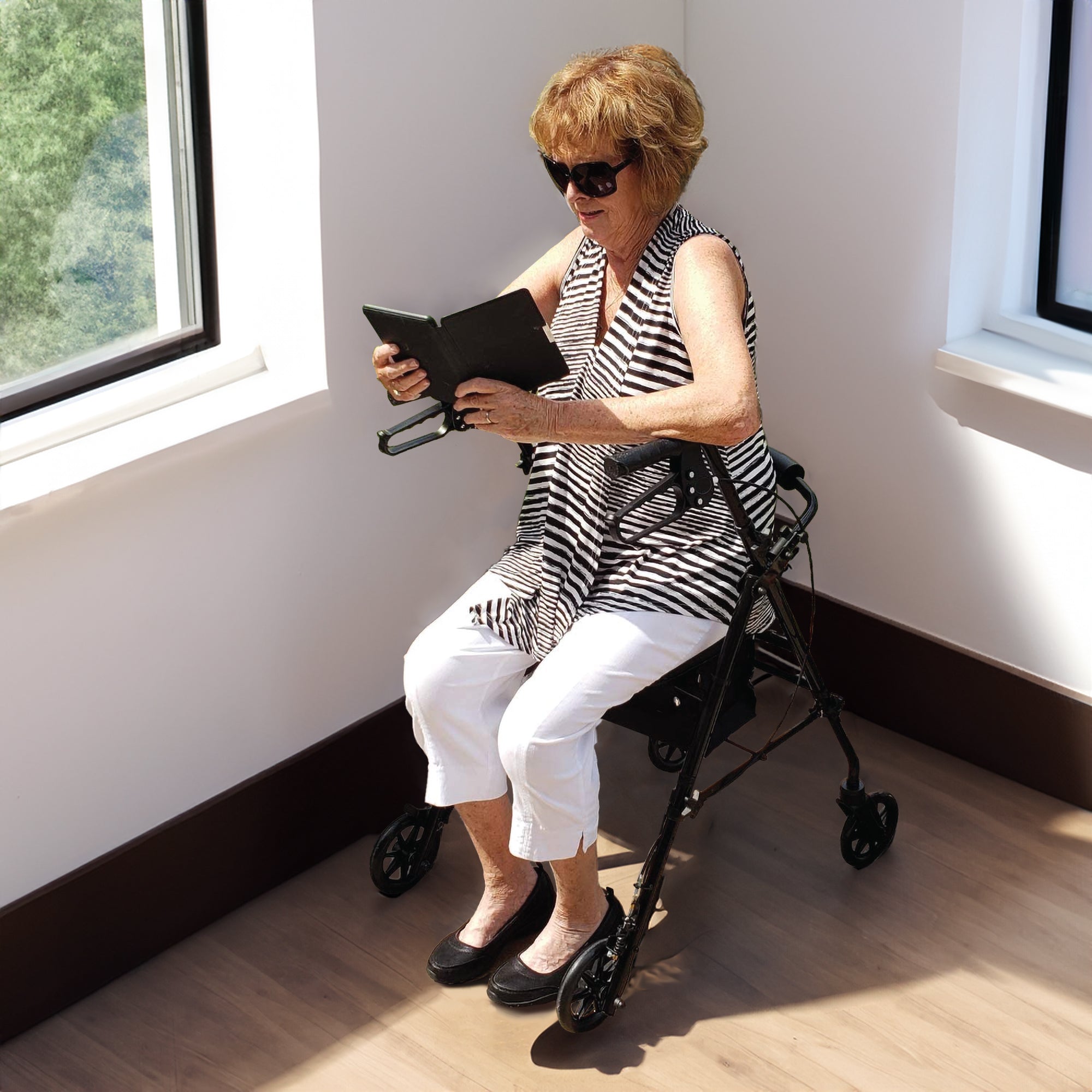 An elderly woman sitting on a rollator reading a tablet