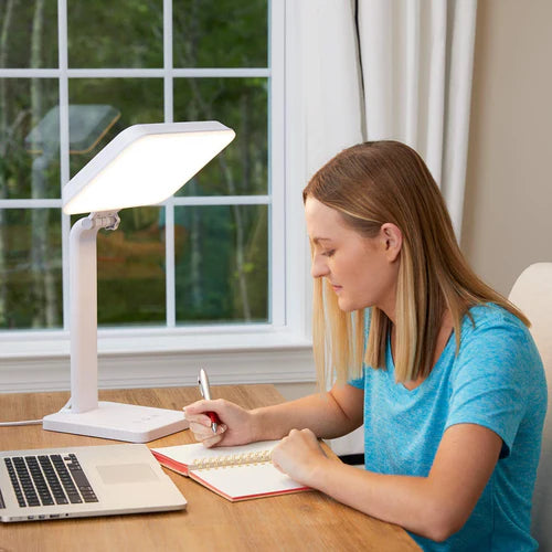 A woman at a desk in front of a therapy lamp