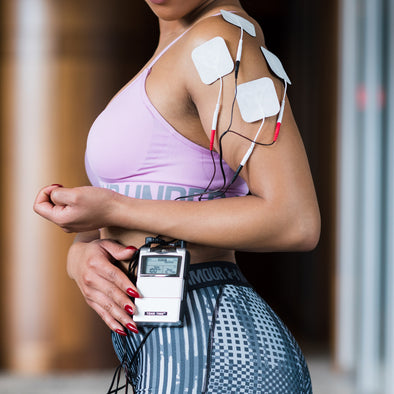 A woman with electrodes on her shoulder and a TENS unit clipped to her waist