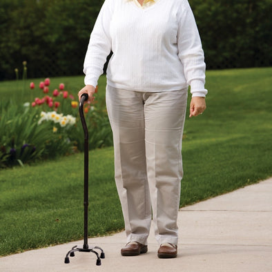 An elderly woman using a quad cane in a park