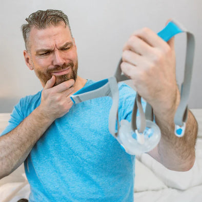 A man with a beard holding a CPAP mask