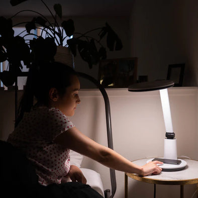 A woman laying in bed turning on a therapy lamp