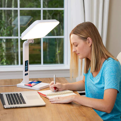 A woman writing at a desk in front of a therapy lamp