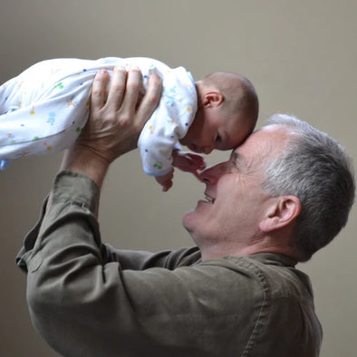 An elderly man holding his grandchild to his head