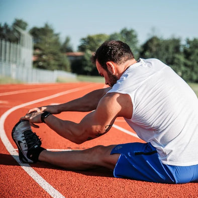 A man sitting down on a track stretching his calf