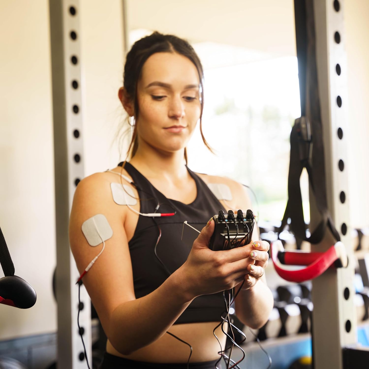 A woman holding a TENS and EMS combo unit in a gym