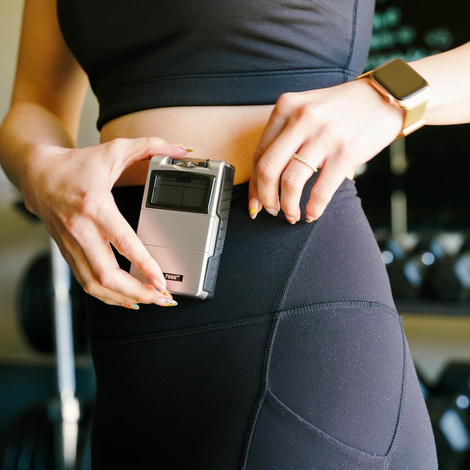 A gray TENS and EMS combo unit being clipped to a woman's pants