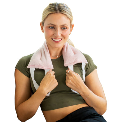 Woman with pink hot and cold therapy wrap on neck and shoulders, wearing green athletic outfit, on white background