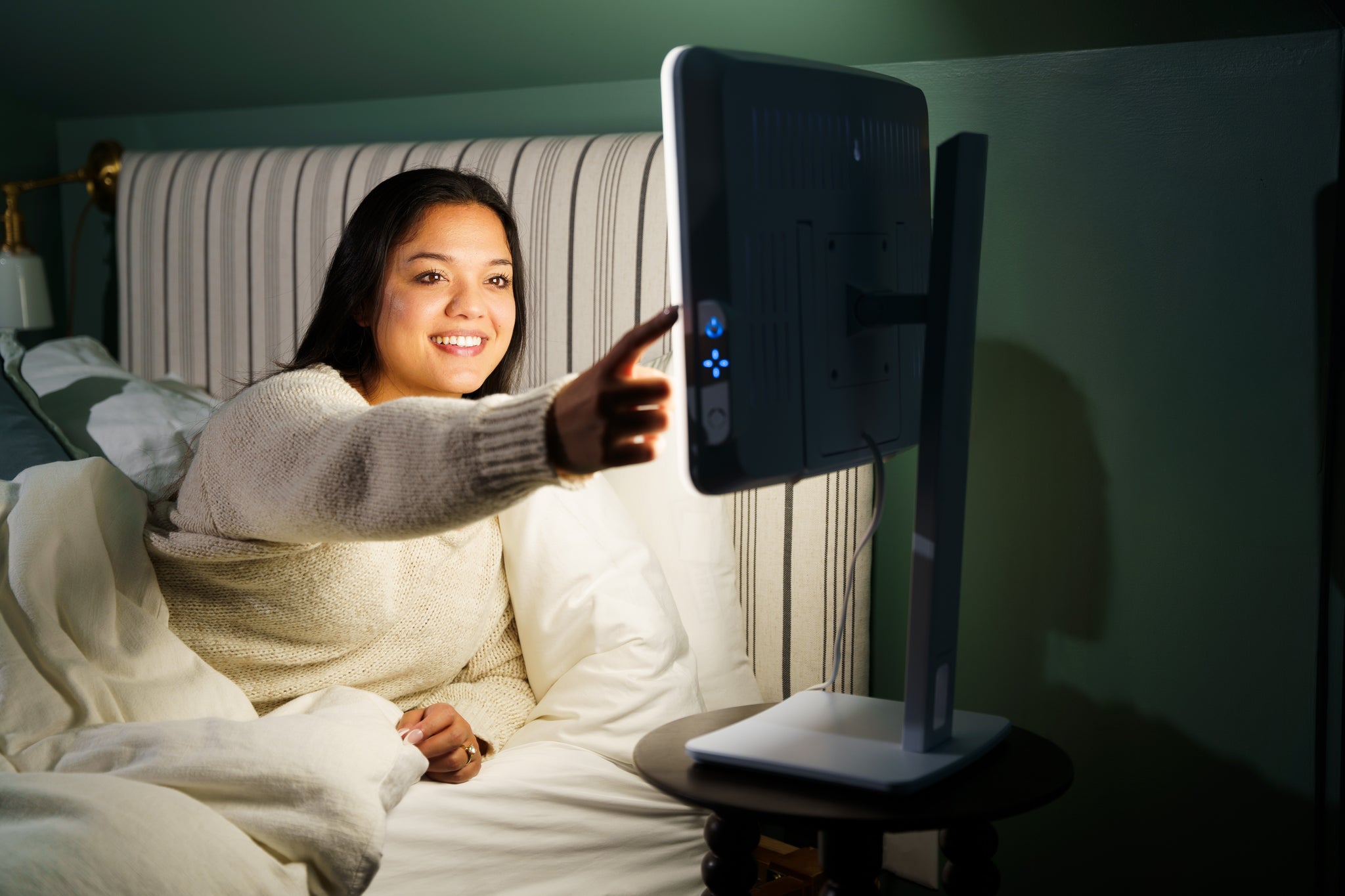A woman pressing the buttons of a therapy lamp while in bed