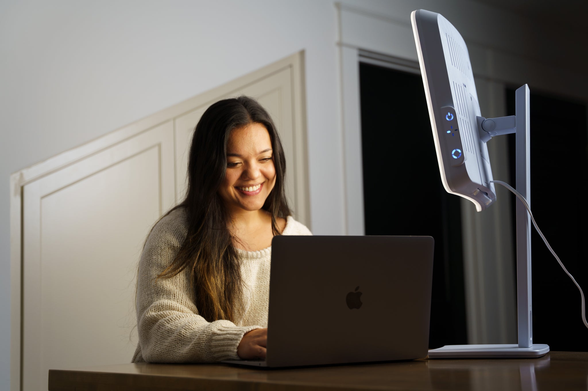 A woman sitting in front of a therapy lamp while on her laptop