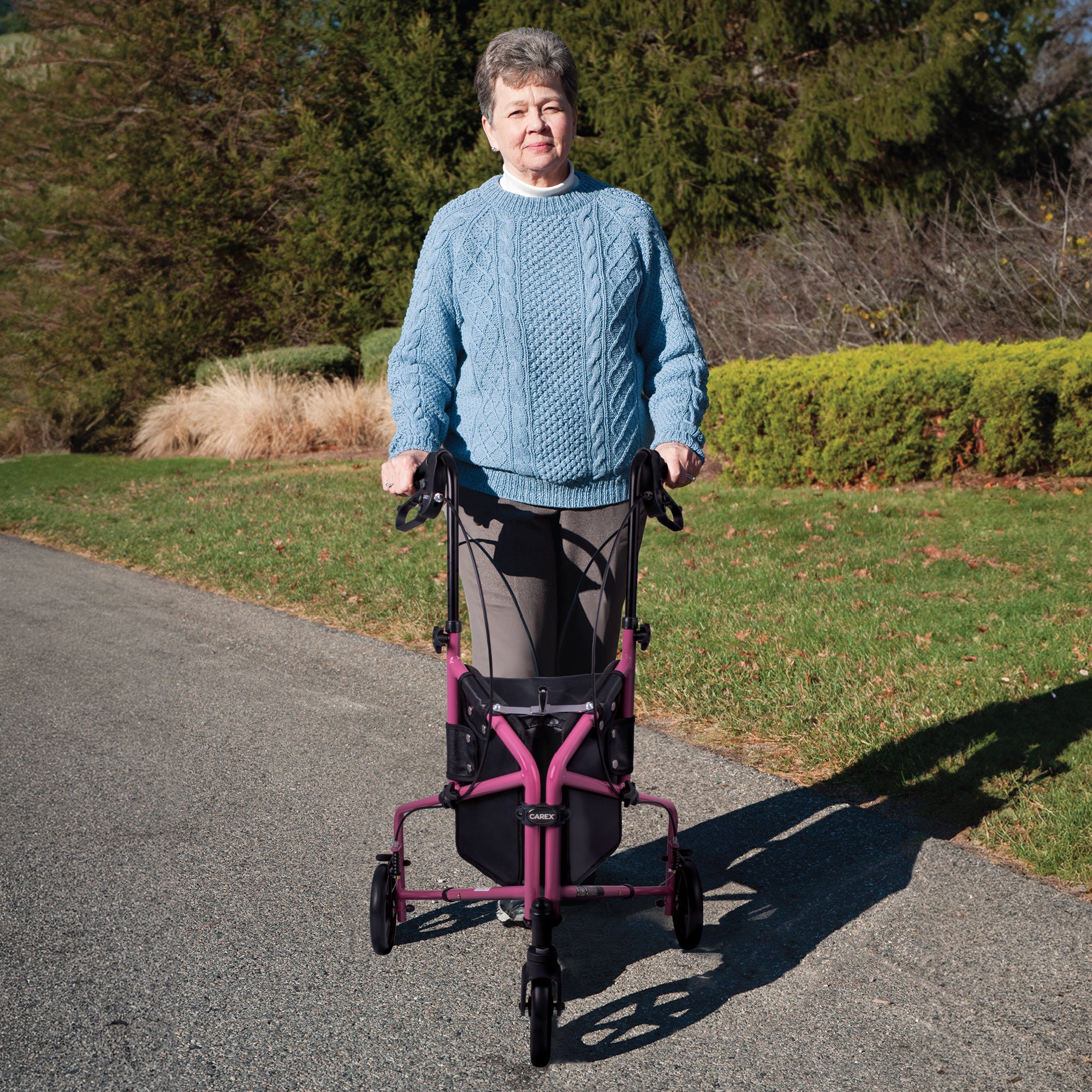 An elderly woman standing with a pink rollator