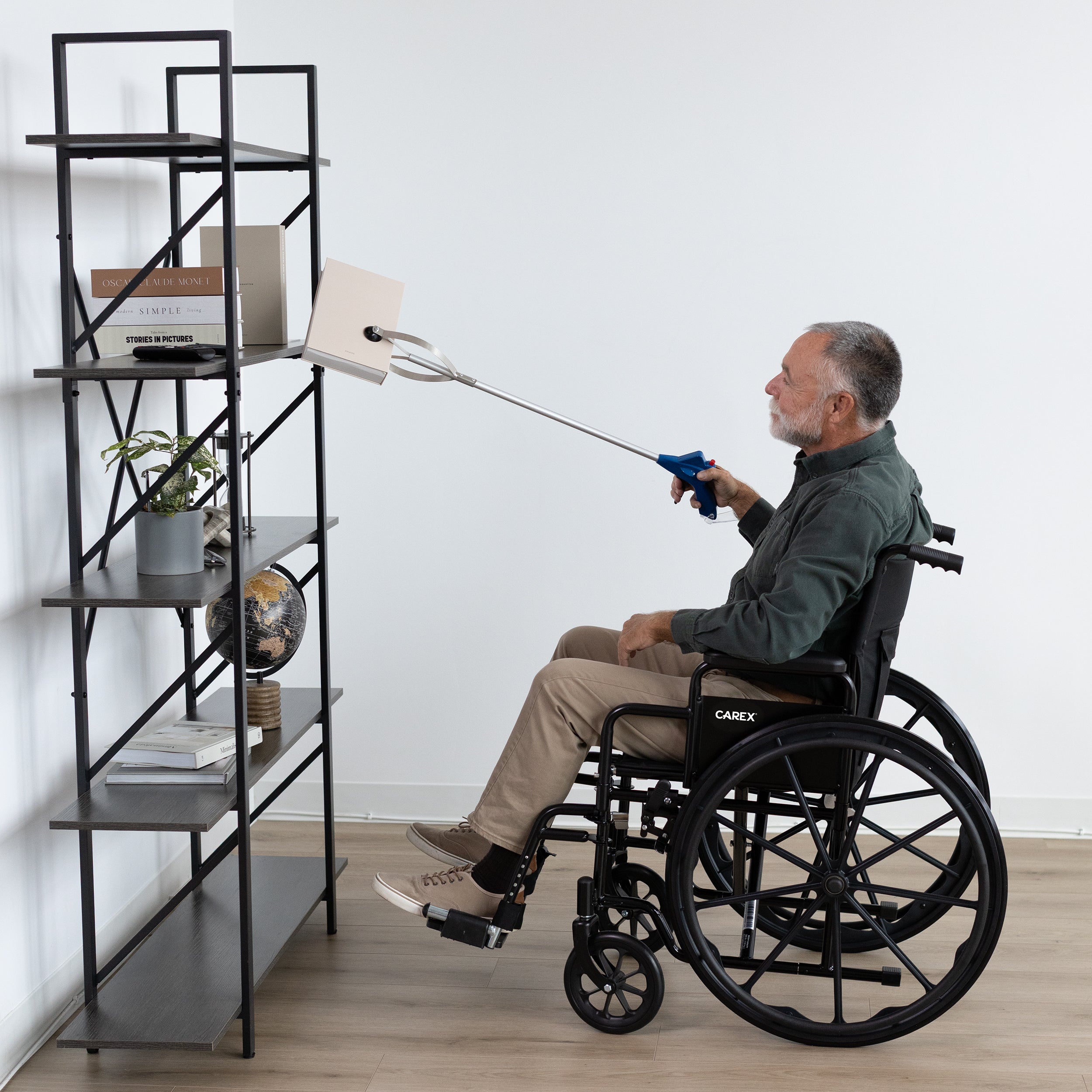 Man in a wheelchair using a reach extension tool to reach items on a high shelf.
